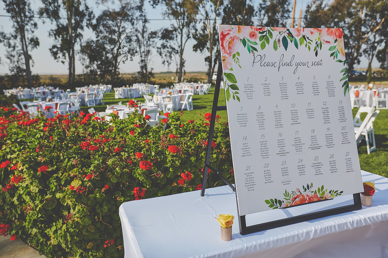 sign on a table that says Please find your seat, followed by a list of table numbers and names